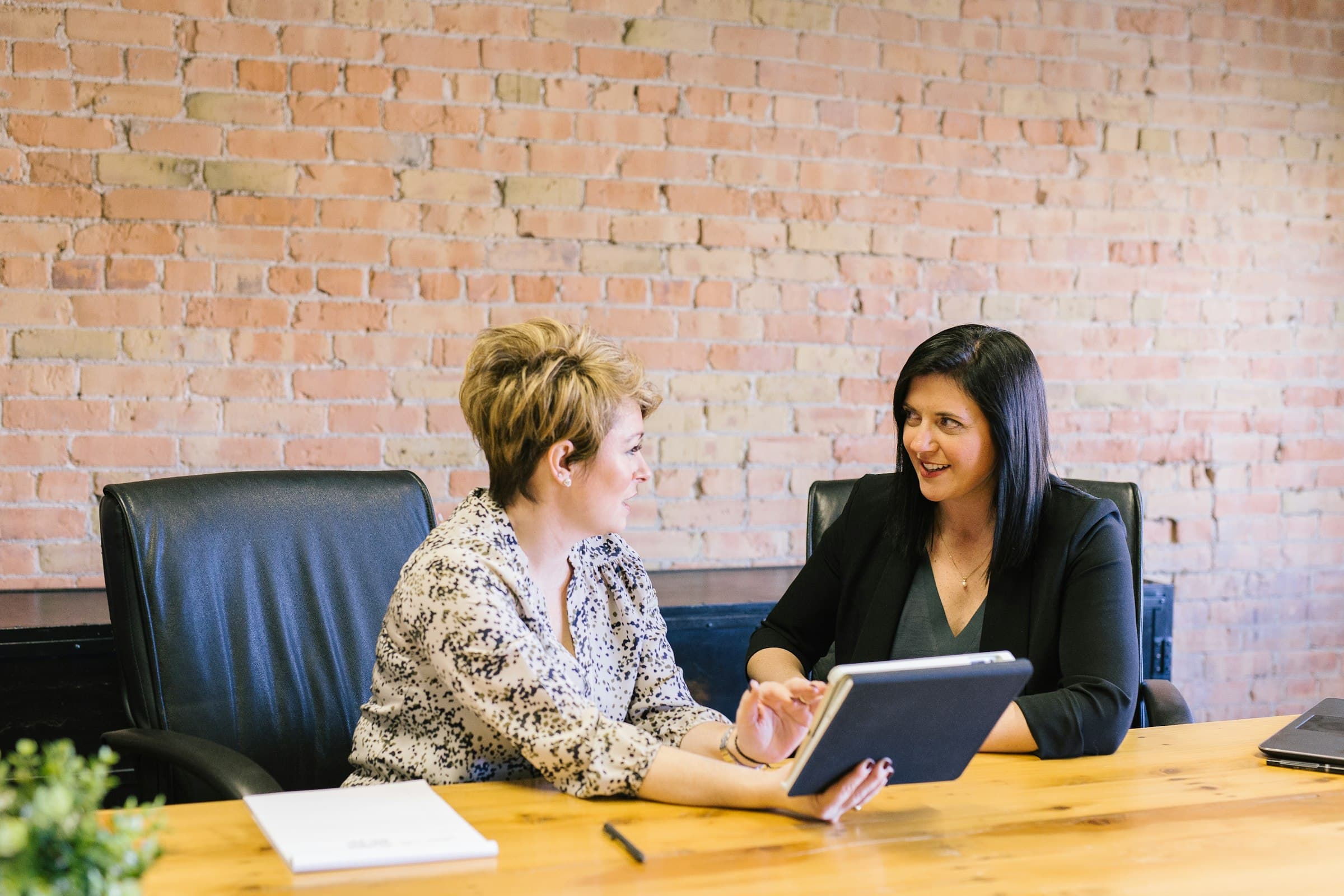 Two colleagues in conversation at a wooden table, one listening